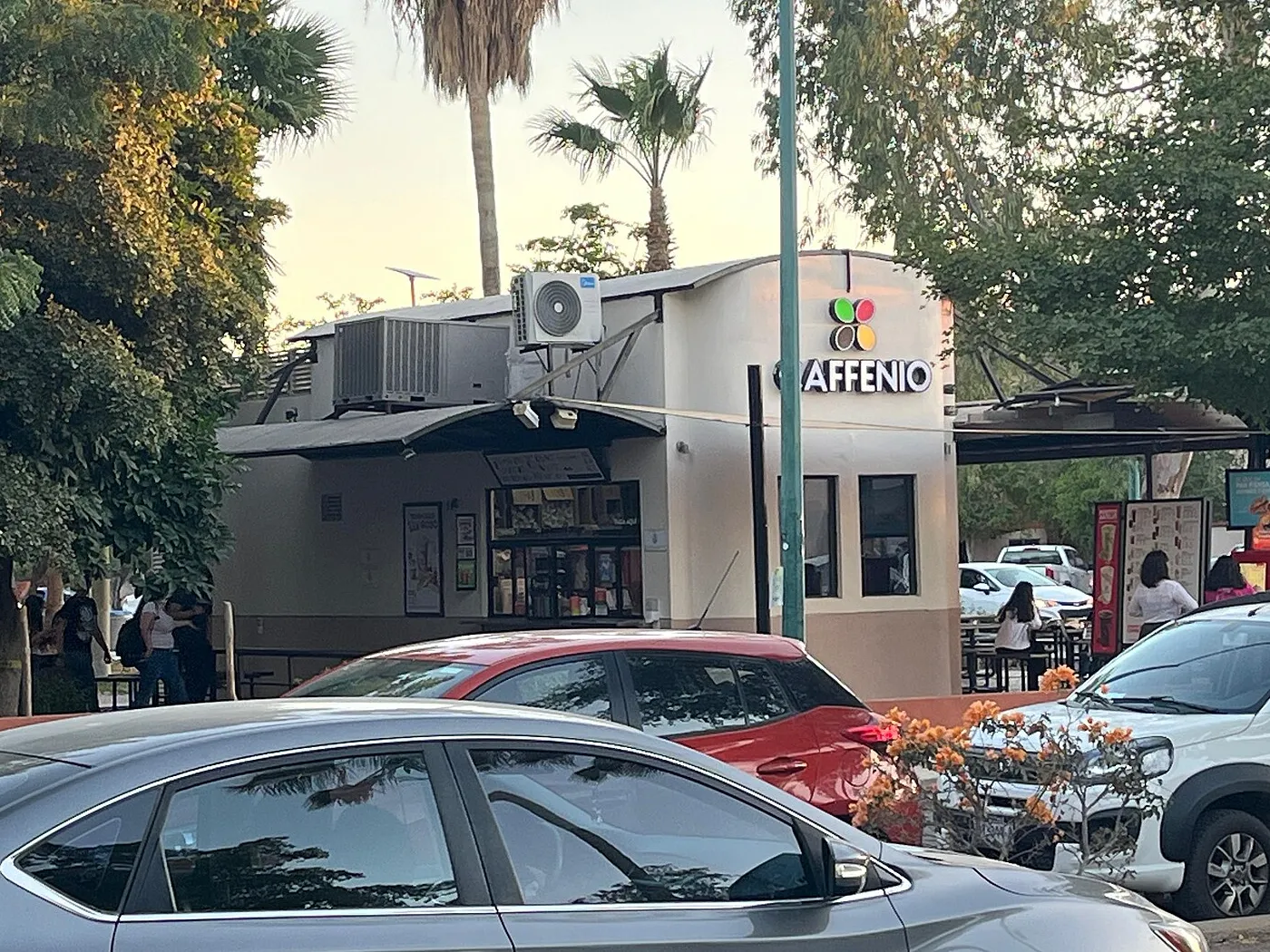 Sucursal de Caffenio en la Universidad de Sonora, en Hermosillo, con el logotipo sobre la ventanilla y autos estacionados al frente.