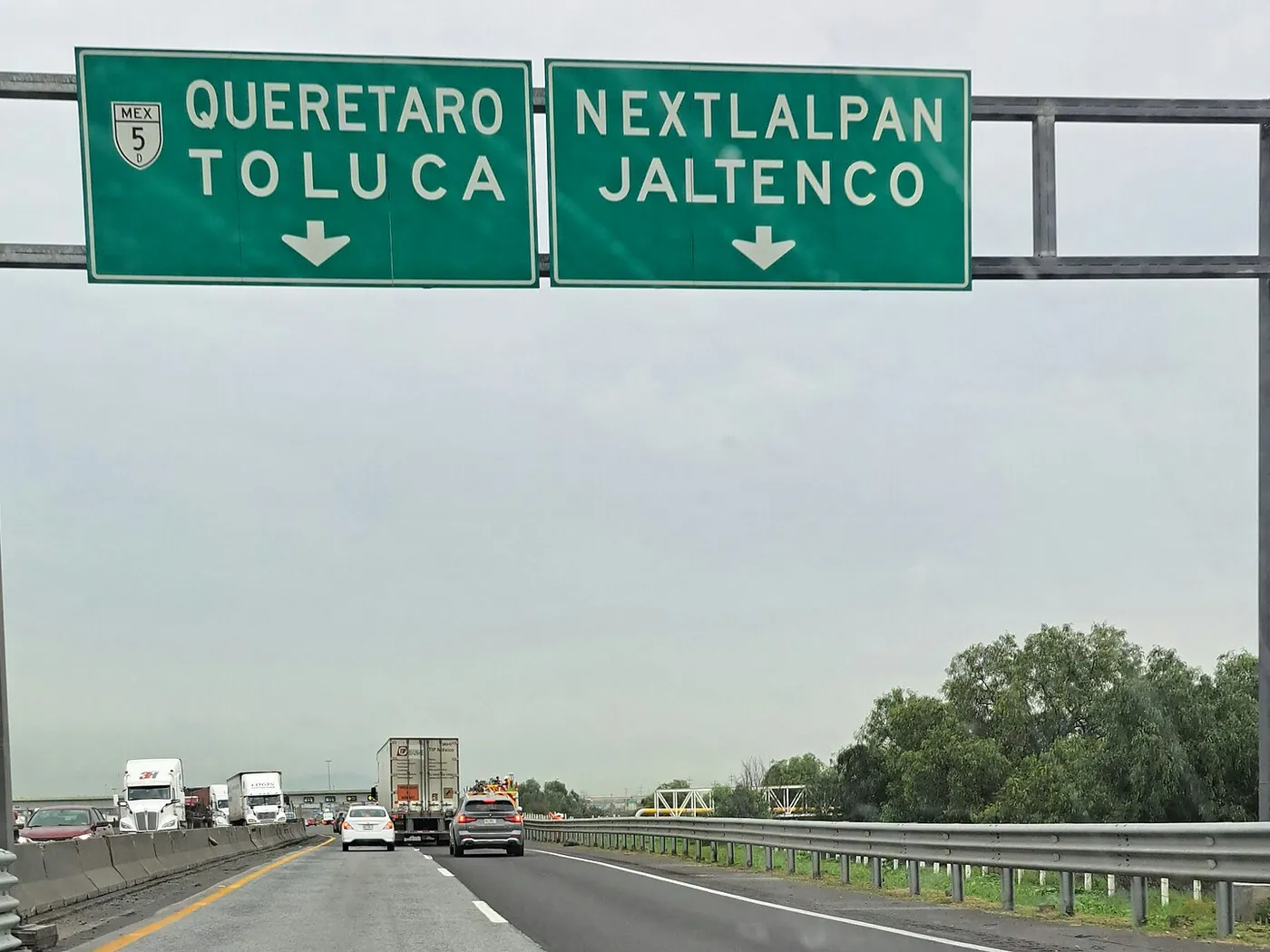 El Circuito Exterior Mexiquense cerca de la caseta de Tultepec, en un día nublado, con tráileres y autos bajo un pórtico de letreros verdes a Querétaro, Toluca, Nextlalpan y Jaltenco.