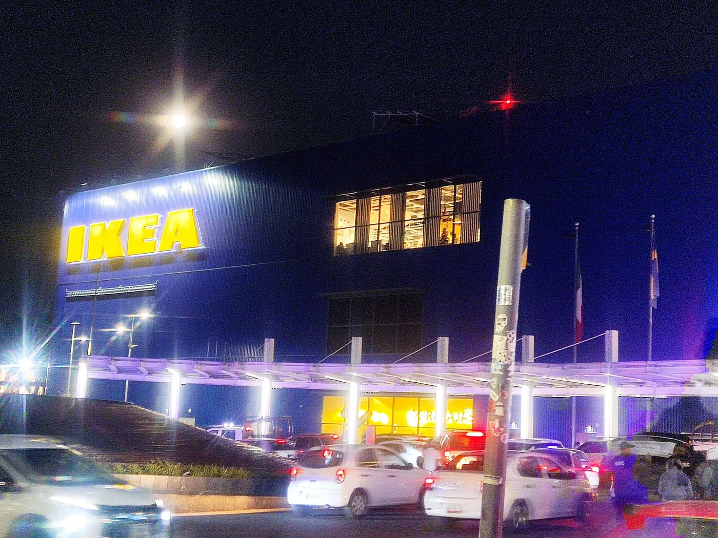 Tienda IKEA Oceanía, en la Ciudad de México, de noche, con el letrero amarillo iluminado sobre la fachada azul y autos en el estacionamiento.