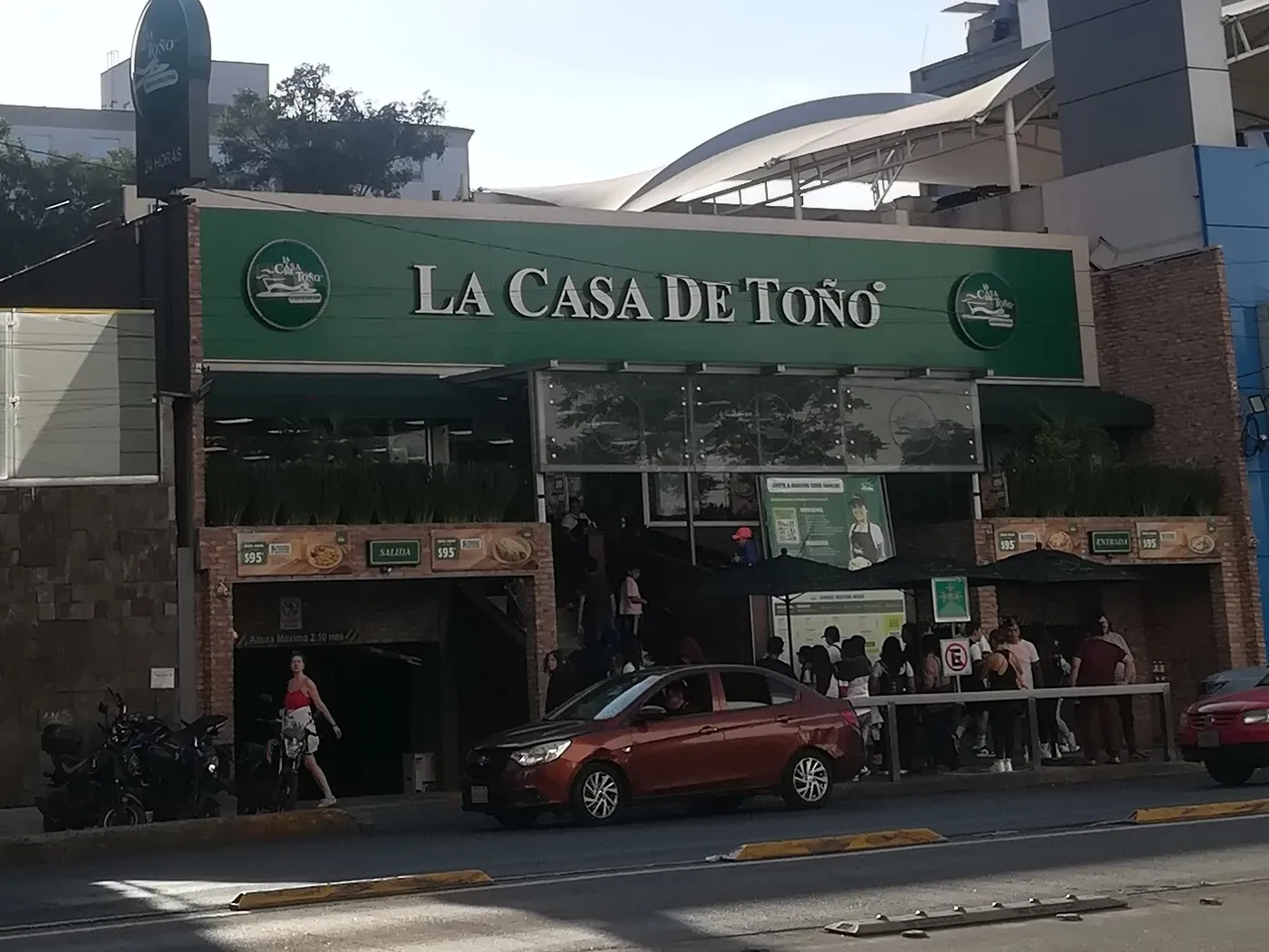 Fachada de La Casa de Toño en la colonia Narvarte, Ciudad de México, con el letrero verde sobre la entrada, la entrada al estacionamiento a la izquierda y gente esperando en la banqueta.