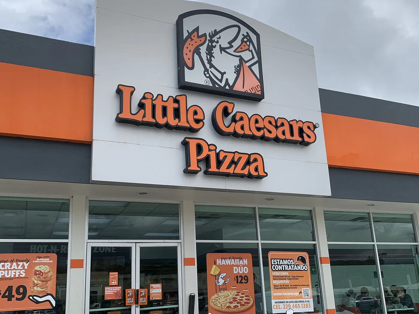 Fachada de una sucursal de Little Caesars Pizza en Xalapa, Veracruz, con el logo del césar sobre el letrero naranja y carteles de promociones en los ventanales.