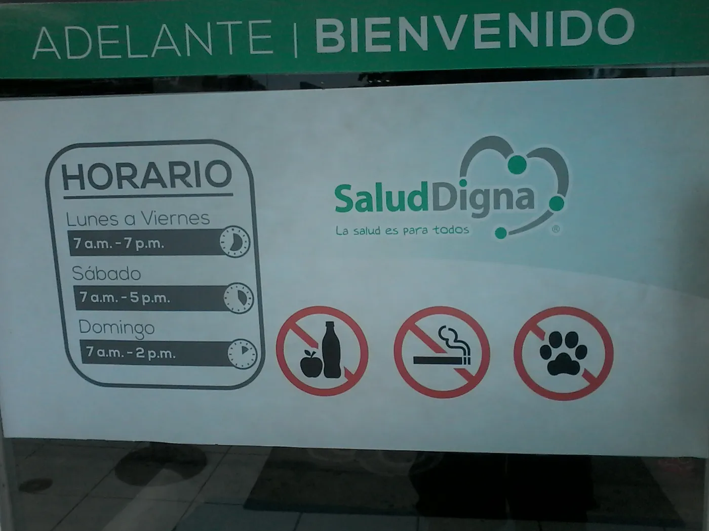 Puerta de cristal de una clínica Salud Digna en Mazatlán, Sinaloa, con el logotipo, el horario y avisos de no entrar con alimentos, fumar ni mascotas.
