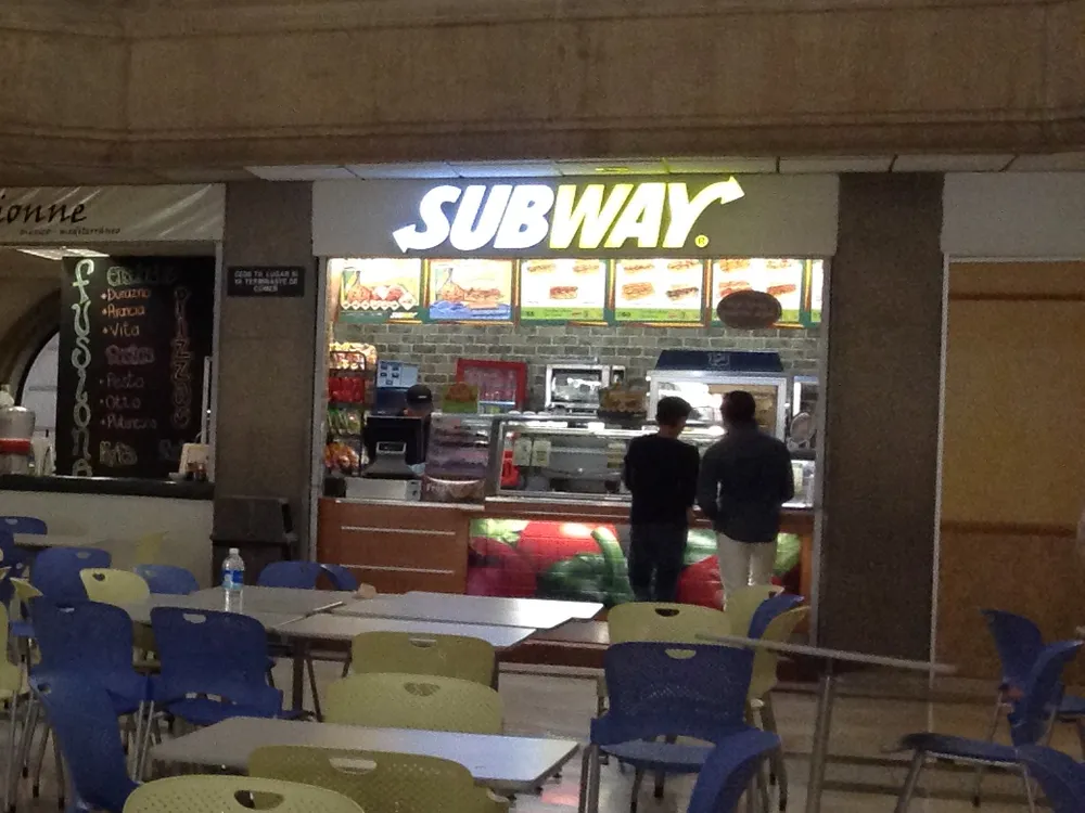 Mostrador de Subway con su letrero iluminado en la cafetería del Tec de Monterrey, Campus Ciudad de México, con mesas y sillas al frente.